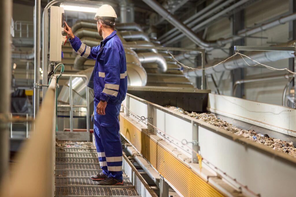 Maintenance worker inspecting a conveyor system in a recycling plant.
